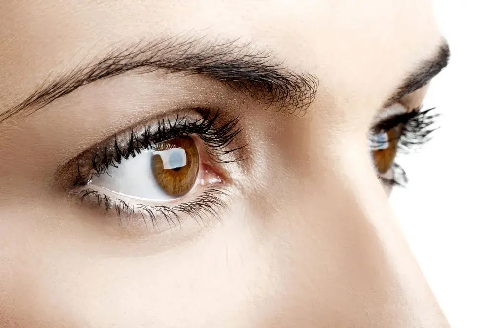 Close-up of a brown eye with long eyelashes against a light background.