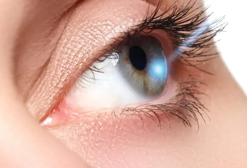Close-up of an eye with a laser beam highlighting the pupil.