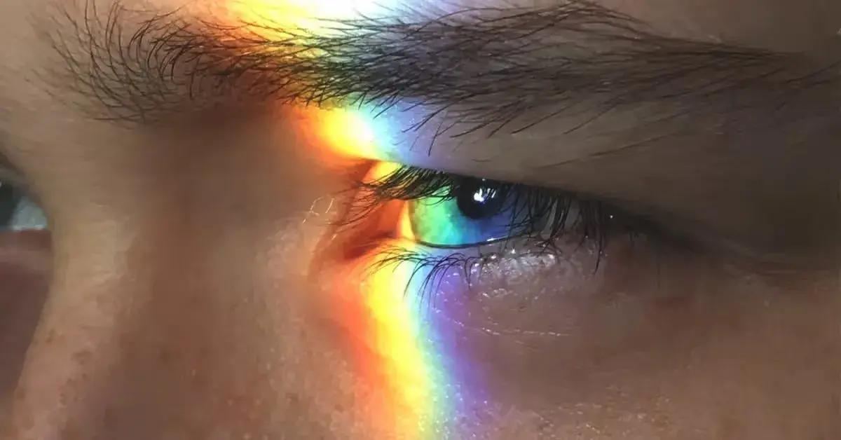 Close-up of a person's eye with a rainbow reflection on the surface.
