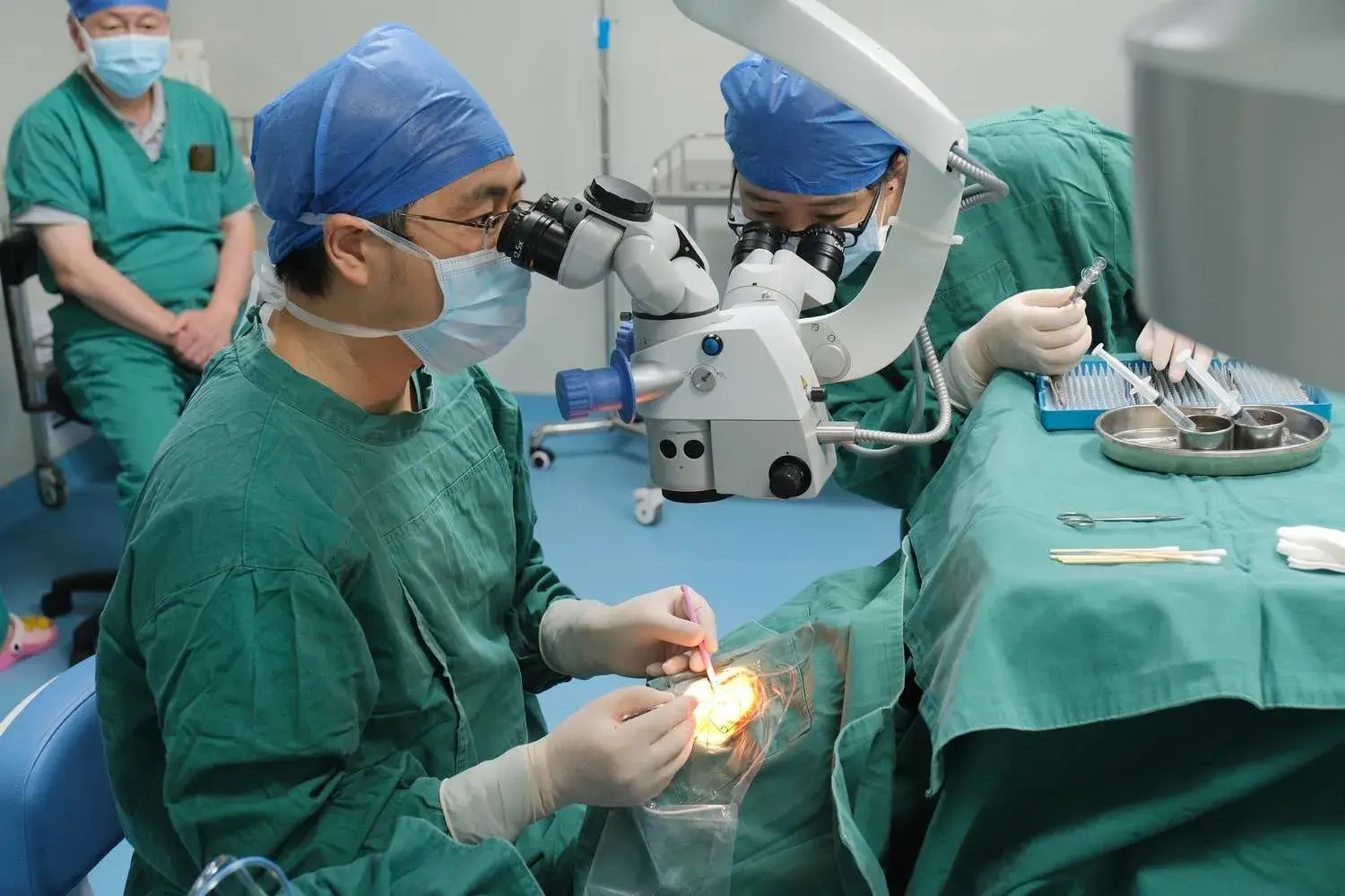Surgeons performing a corneal surgical procedure, with instruments and eye microscope present.