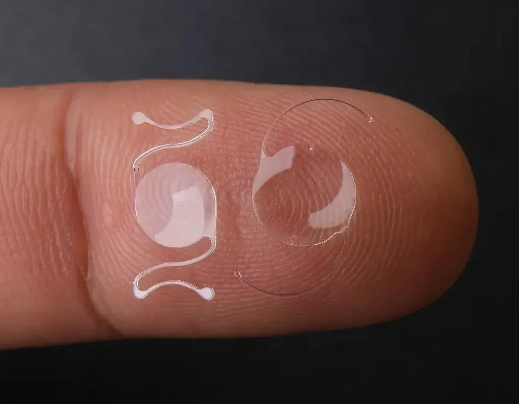 Two replacement lenses displayed on a fingertip against a dark background.