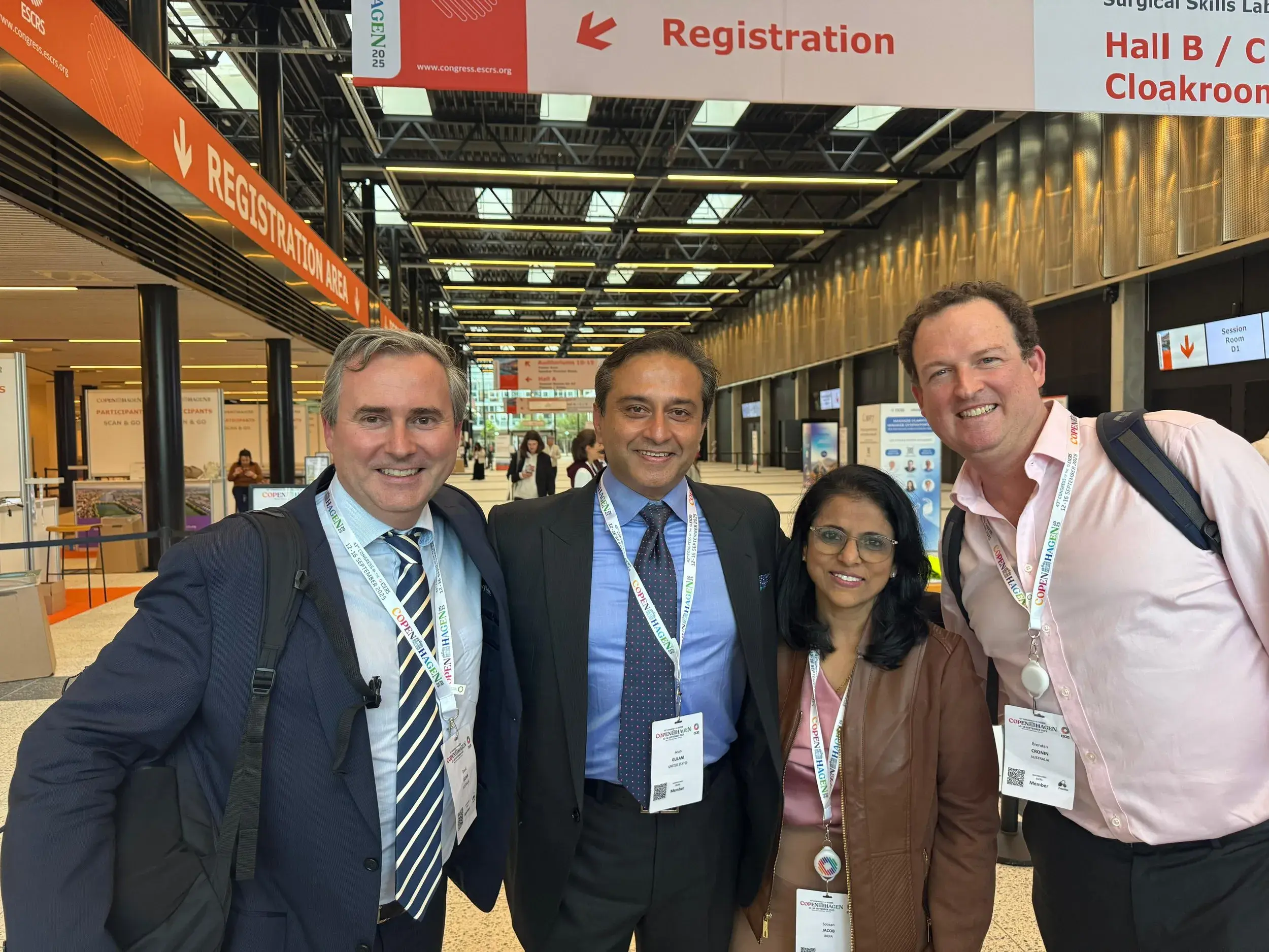 Four smiling individuals in business attire at the ESCRS registration area.