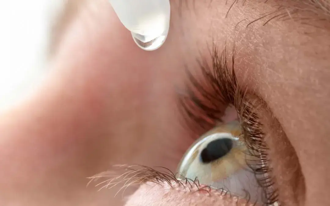 Close-up of an eye with a dropper applying eye drops.