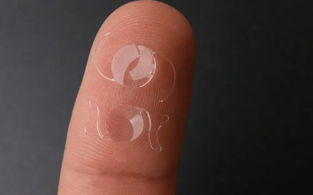 Close-up of a clear intraocular lens resting on a fingertip.
