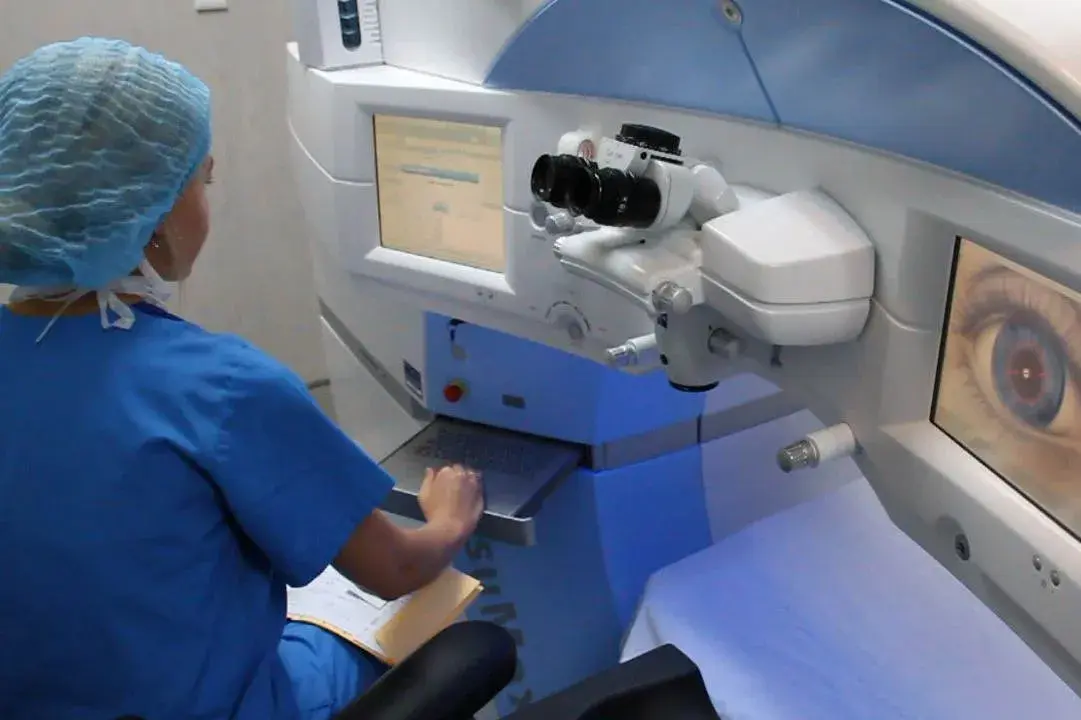 Operator preparing laser eye surgery equipment with screens displaying eye anatomy.