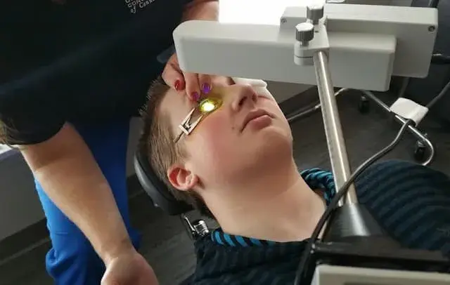 Patient undergoing corneal examination with a light device.