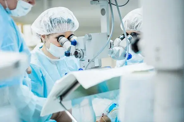 Surgeons in scrubs using a surgical microscope during cataract surgery.