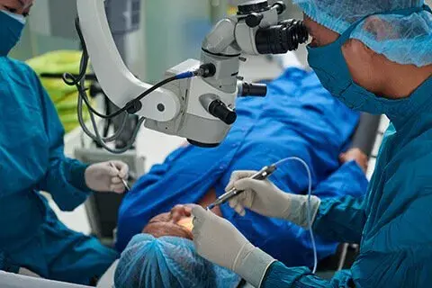 Surgeons performing a corneal surgery with a microscope on a patient.