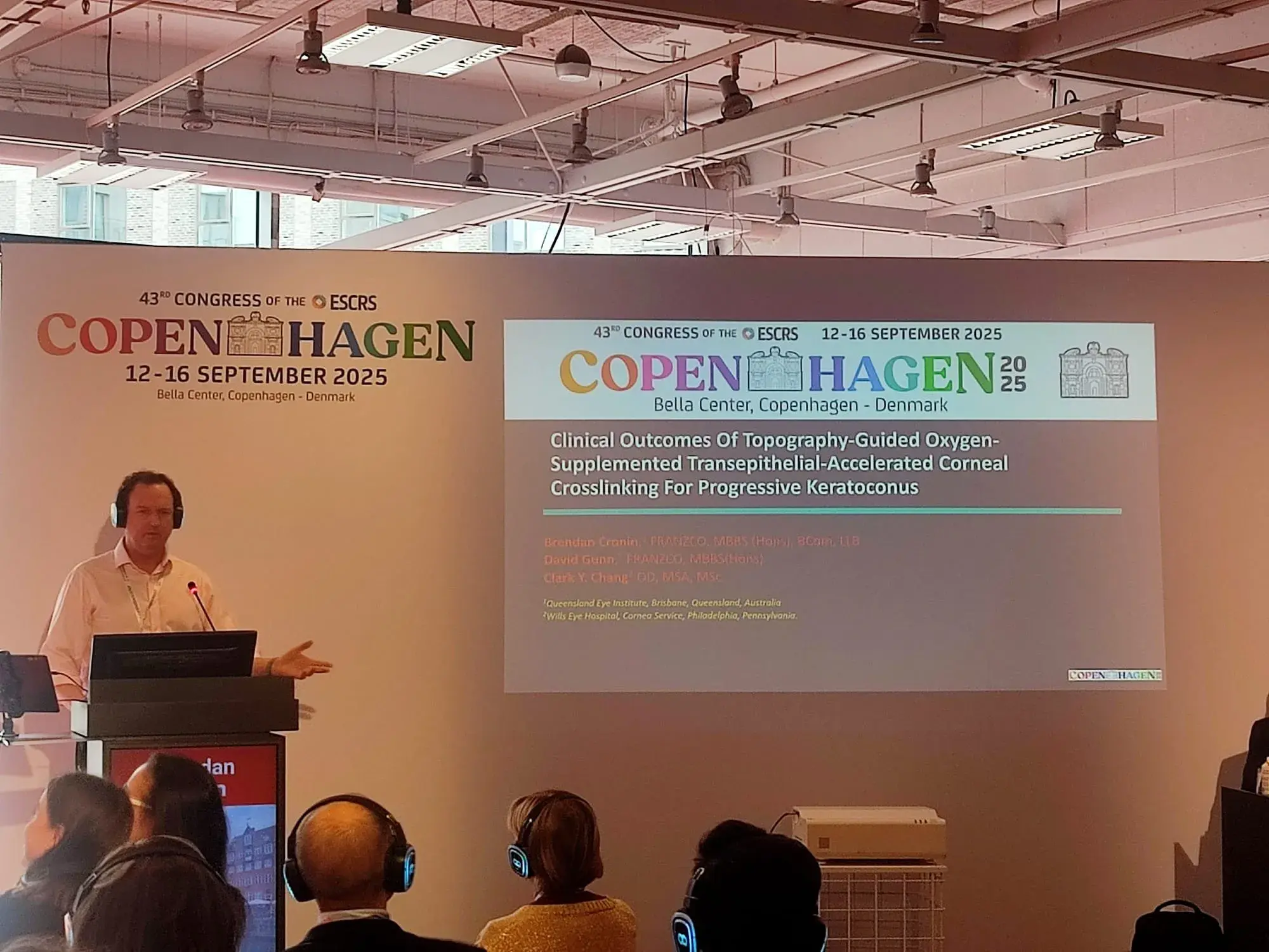 Speaker presenting at ESCRS congress in Copenhagen, 2025, with audience in headphones.