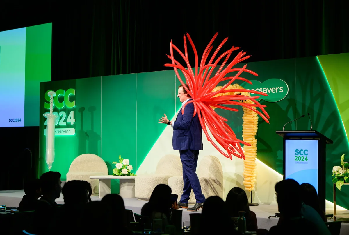 Dr Brendan Cronin presenting with a red balloon sculpture at Specsavers Clinical Conference 2024